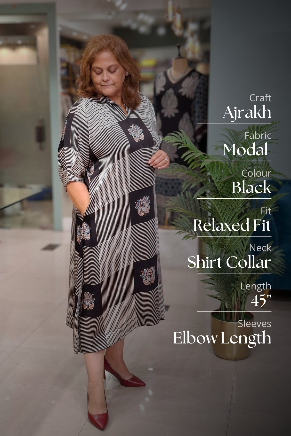 A woman modeling a gray and black checkered Ajrakh fabric dress with floral motifs, standing in a boutique setting with text overlays detailing the garment's features.