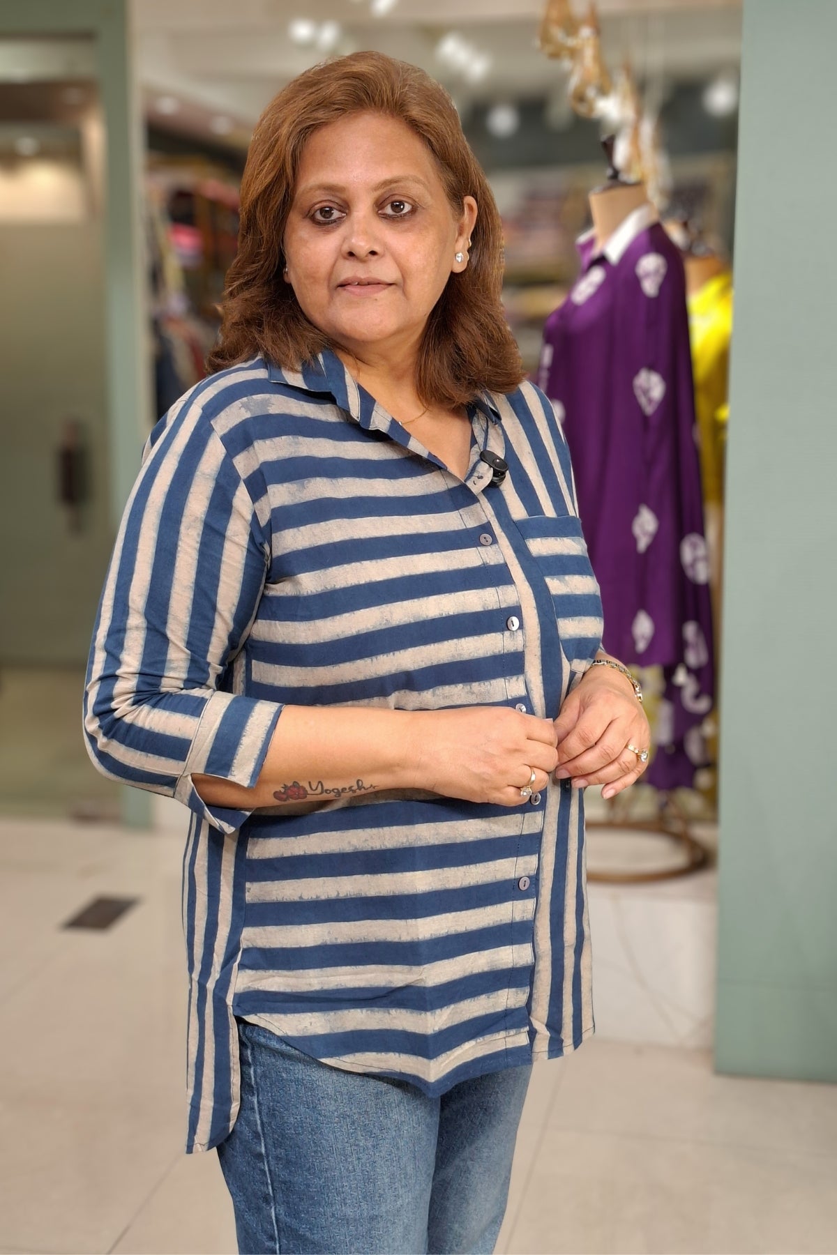 A woman wearing a blue and off-white striped long-sleeve button-up shirt with blue jeans, standing in a retail store.