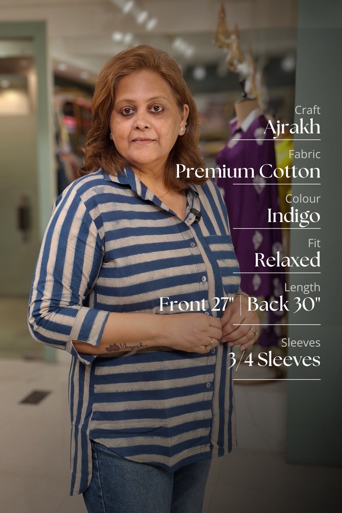 A woman modeling a blue and white striped relaxed-fit cotton shirt in a retail store setting, with product specifications text overlaid on the right side.