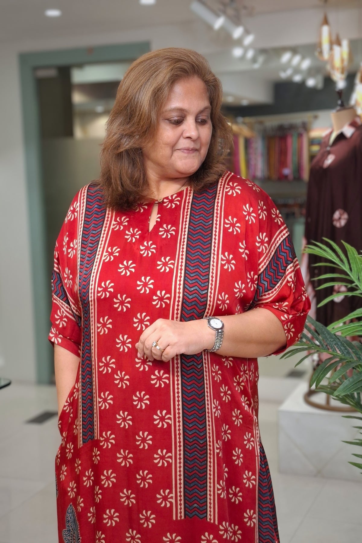 A woman wearing a red kurta with white floral patterns and blue vertical stripes, standing in a clothing store.