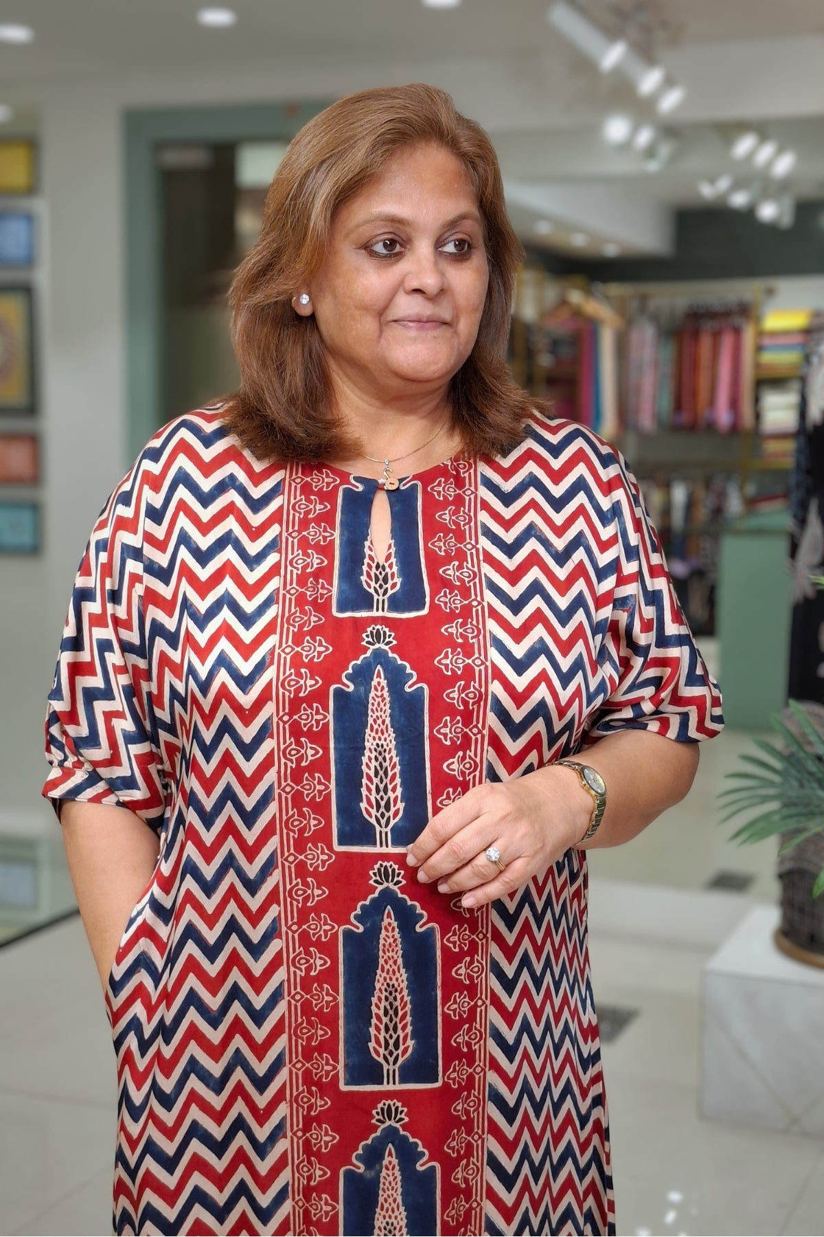 A woman wearing a red, navy, and white patterned tunic top with vertical chevron and arch motifs, standing in a retail store environment.