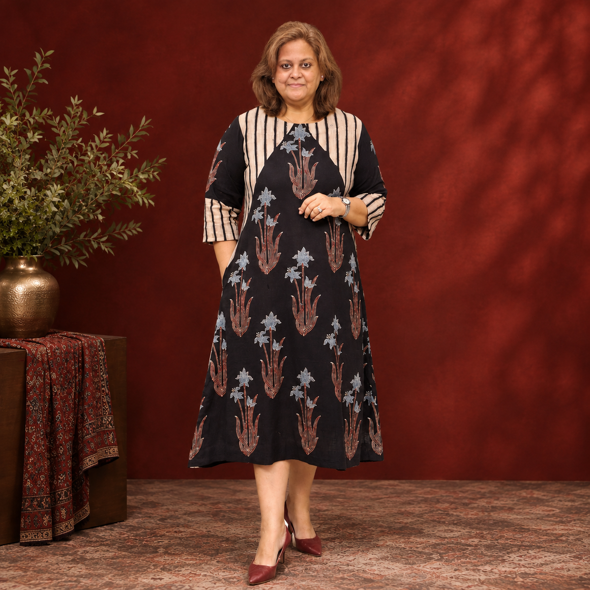 Bellezon woman wearing a black floral printed dress with beige striped detailing and burgundy heels.