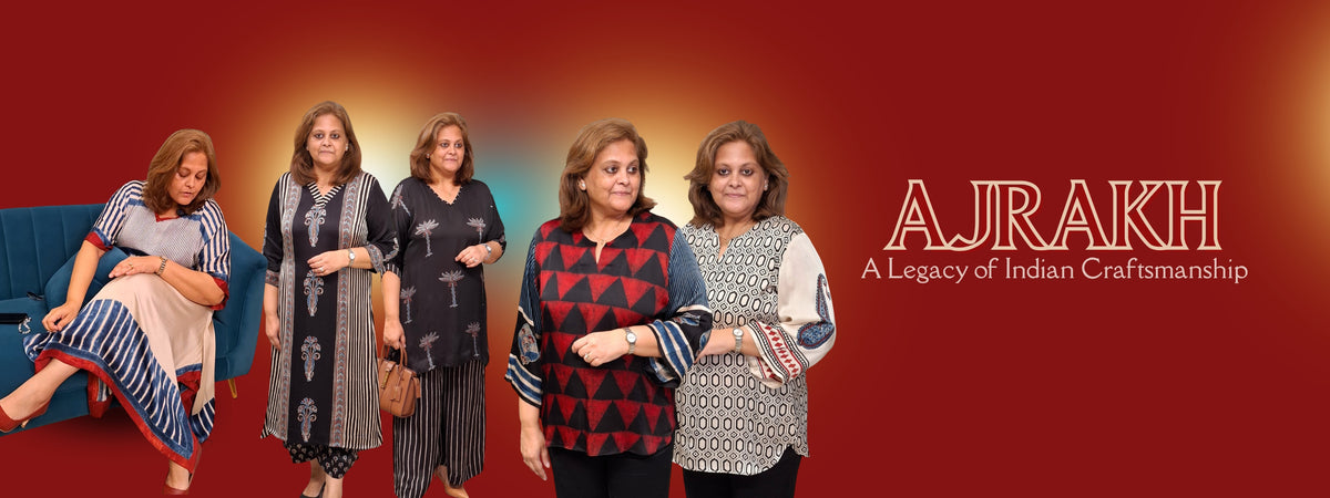 A promotional banner for 'AJRAKH A Legacy of Indian Craftsmanship' featuring five women modeling traditional Indian garments against a warm red gradient background. The text on the right displays the brand name 'AJRAKH' in white with a gold outline.