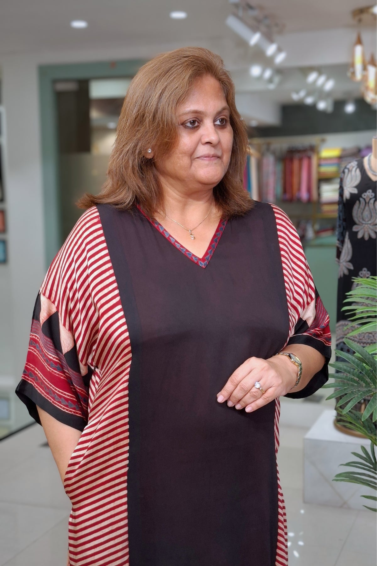A woman wearing a dark brown and red striped tunic dress with a solid dark brown front panel, standing in a clothing store.