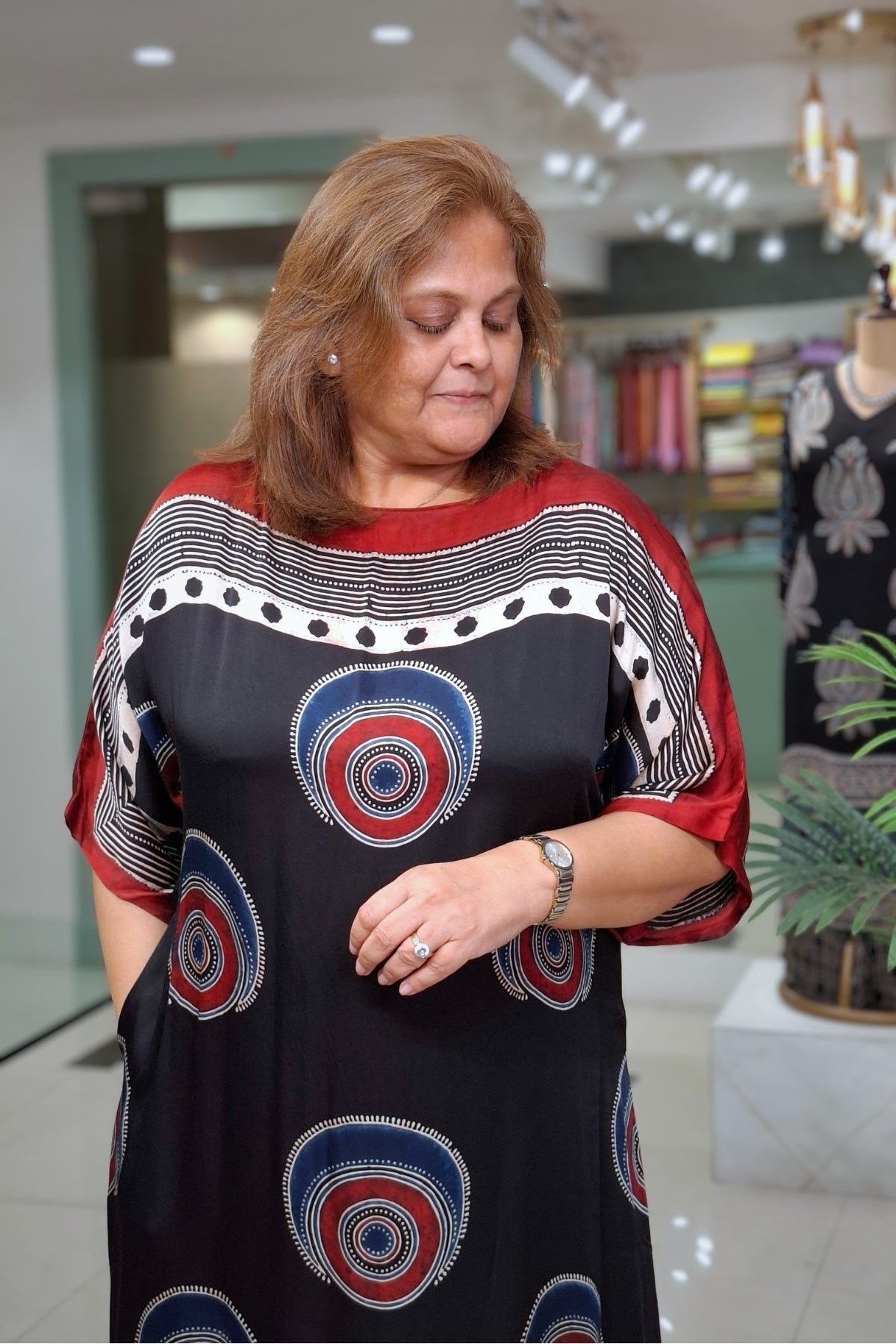 A woman wearing a black tunic dress with red, white, and blue circular patterns, standing in a boutique store.