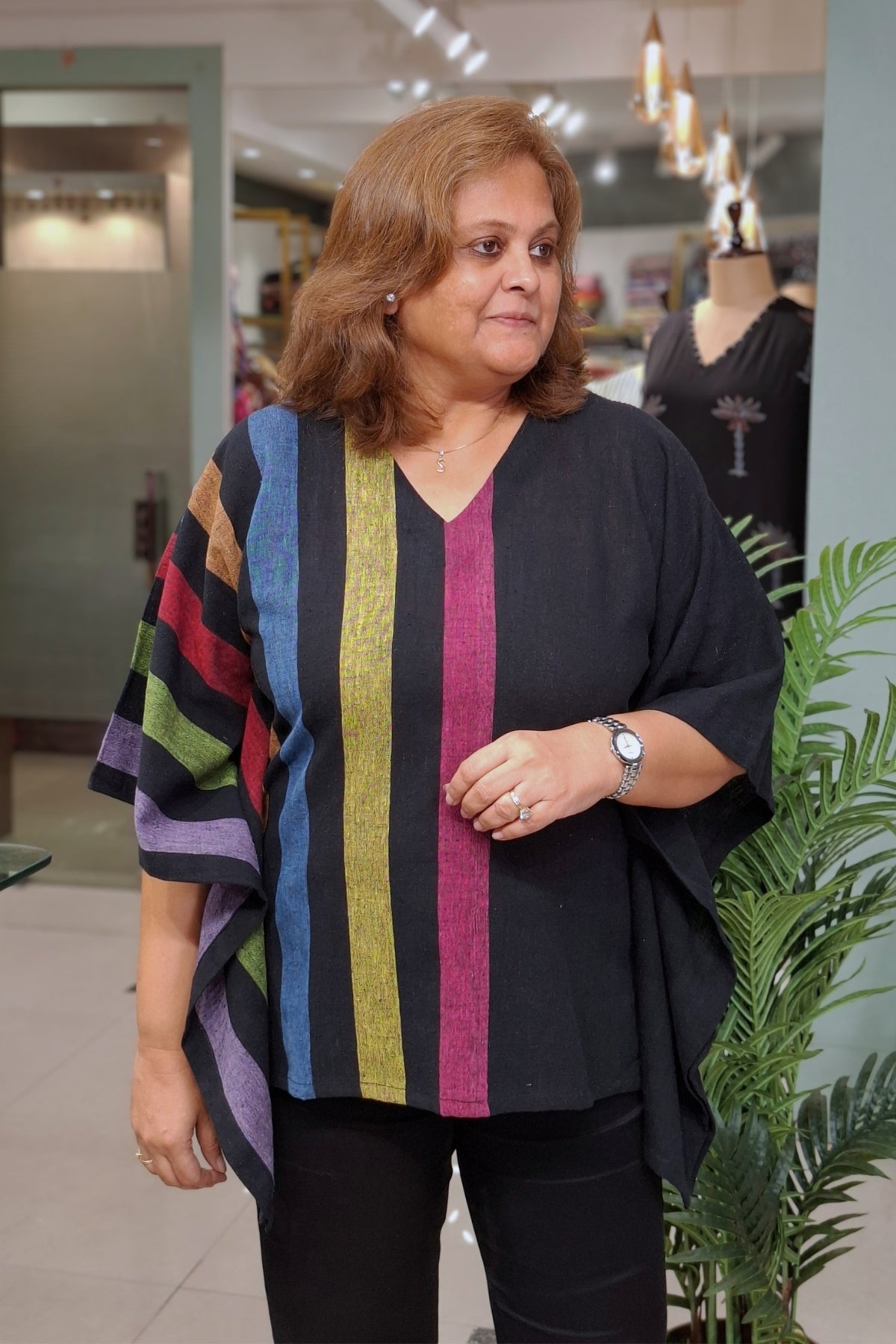 A woman wearing a black V-neck top with vertical stripes in blue, yellow, pink, green, and brown, standing in a retail store.