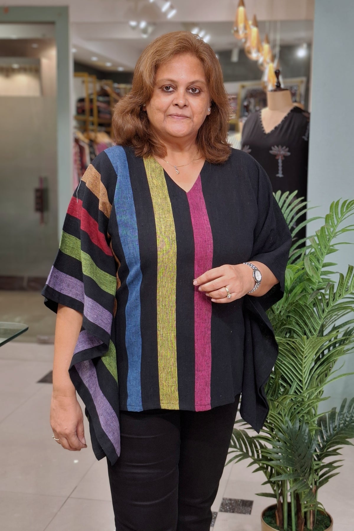 A woman wearing a black V-neck top with vertical multicolor stripes in blue, green, yellow, pink, and purple, paired with black pants, standing in a retail store.