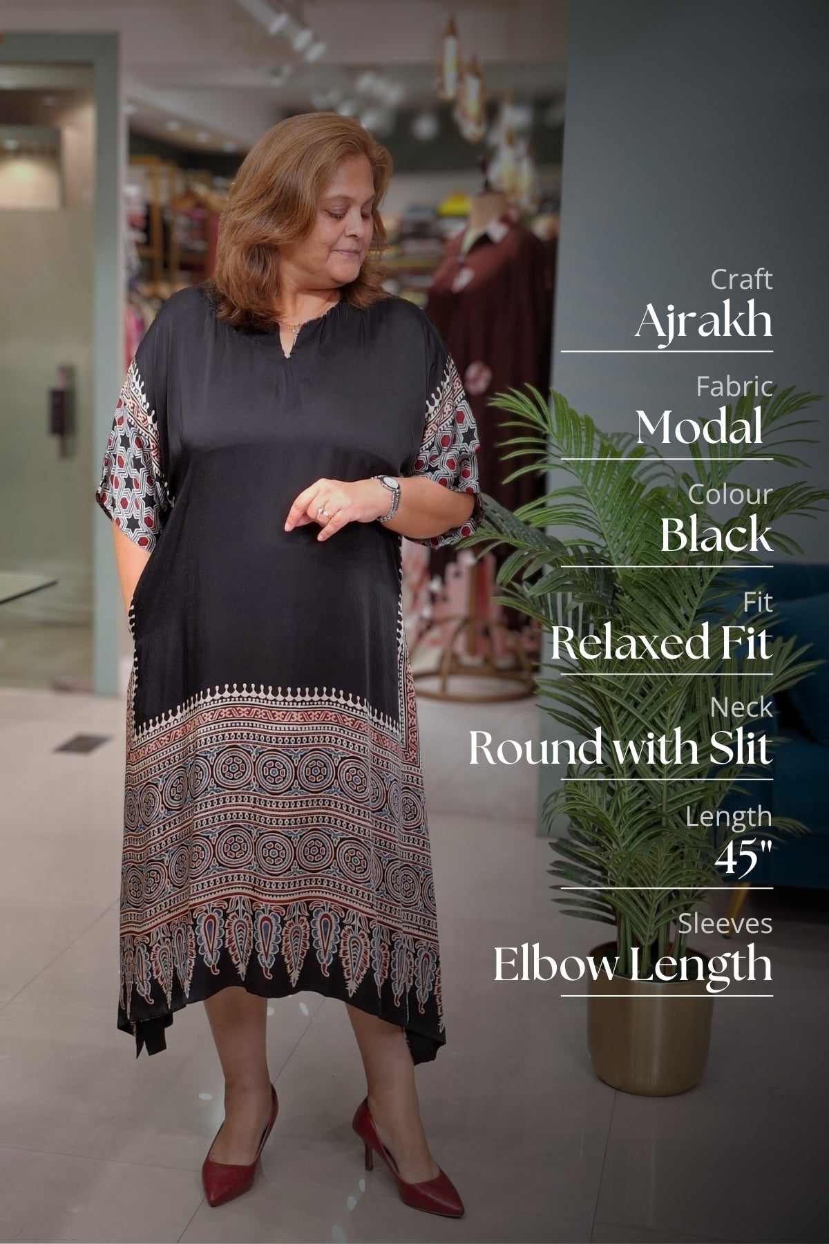 A woman modeling a black Ajrakh kurta with intricate multicolor geometric patterns along the hem and elbow-length sleeves, set in a boutique with text overlays detailing the product features.