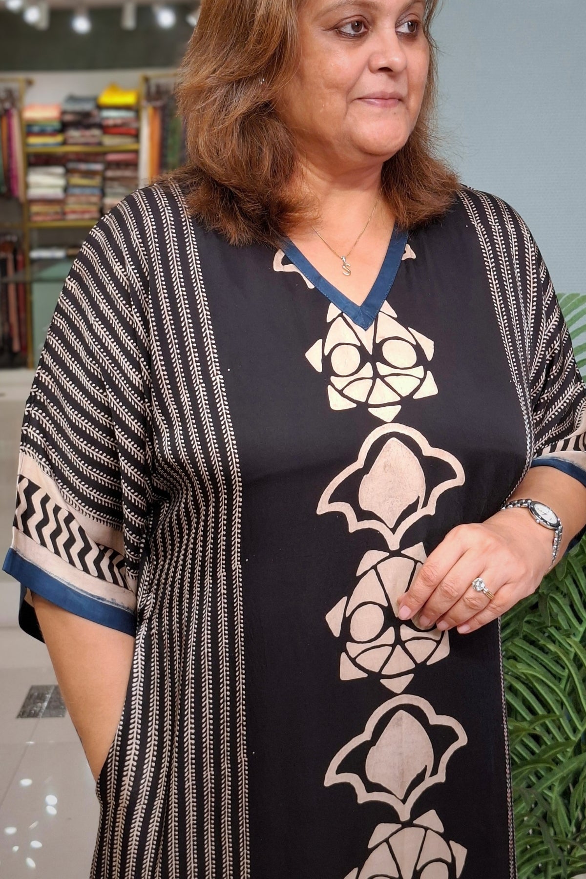 A woman wearing a black V-neck tunic dress with beige geometric patterns and striped sleeves, standing in an indoor setting.